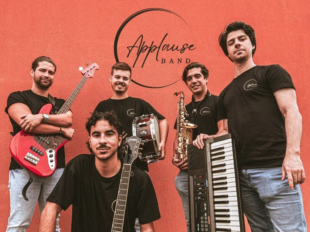 Cinco músicos da Applause Band com instrumentos, diante de fundo alaranjado.