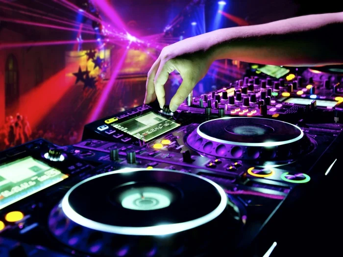 Mesa de DJ e controladores iluminados numa pista de dança.